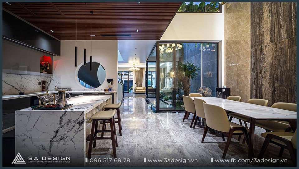 Phòng bếp và bàn ăn hiện đại với đá vân mây, ánh sáng tinh tế, trần gỗ lam và không gian mở ra khu tiểu cảnh xanh.