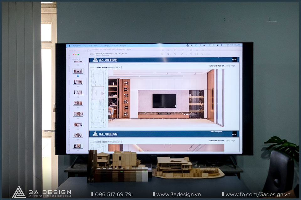 Bản vẽ thiết kế 3D nội thất phòng khách đang được hiển thị trên màn hình lớn, với hai mô hình kiến trúc nhỏ đặt phía dưới, thể hiện quá trình thiết kế và mô phỏng chi tiết trước khi thi công.