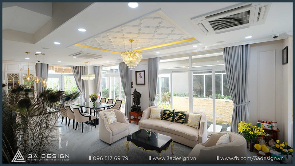 Phòng khách và phòng ăn tân cổ điển với sofa be, bàn ăn trắng và đèn chùm lộng lẫy.