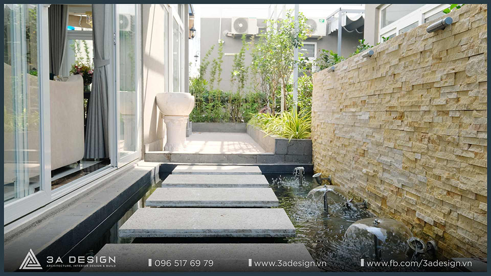 Tiểu cảnh nước và tường ốp đá. Sân vườn lớp đệm với lối đi lát đá kết nối với cửa kính trượt vào nội thất, tuân thủ phong thủy.