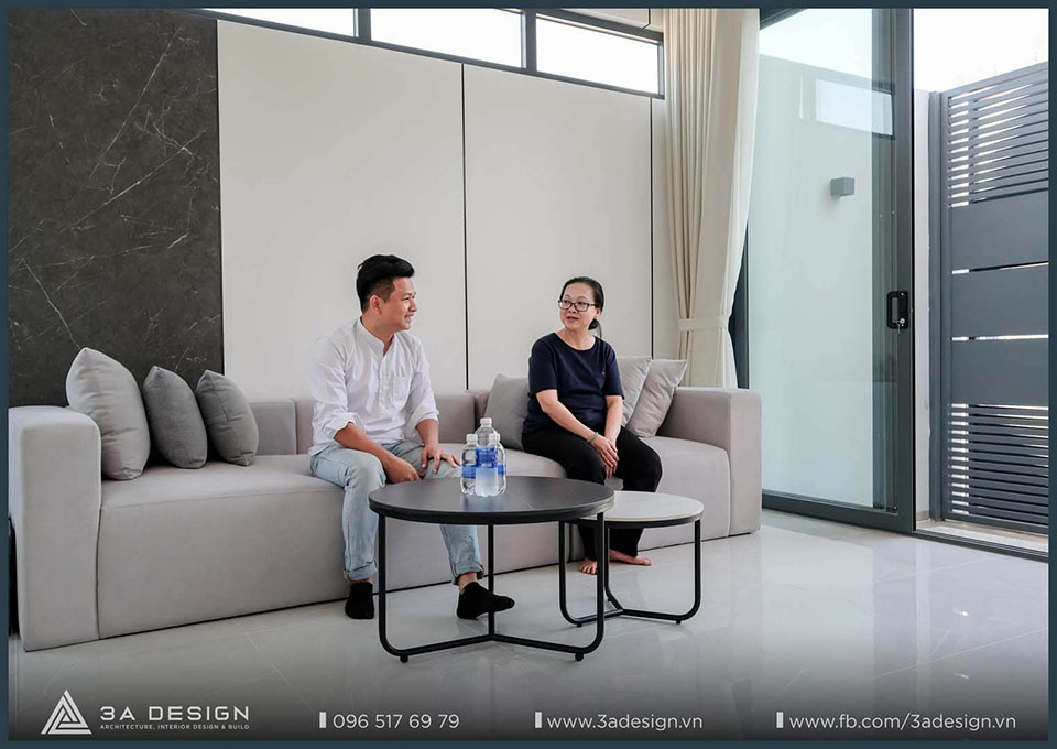 Một kiến trúc sư 3A Design trò chuyện thân tình với gia chủ trên sofa trong không gian nhà phố hiện đại, thể hiện sự quan tâm đến trải nghiệm sống của khách hàng.